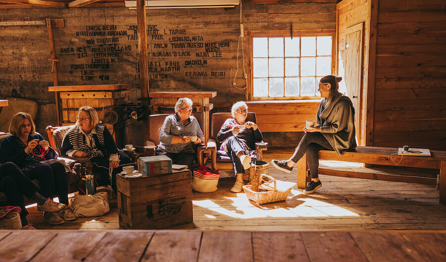 a group of women sitting, chatting and laughing, inside a woolshed