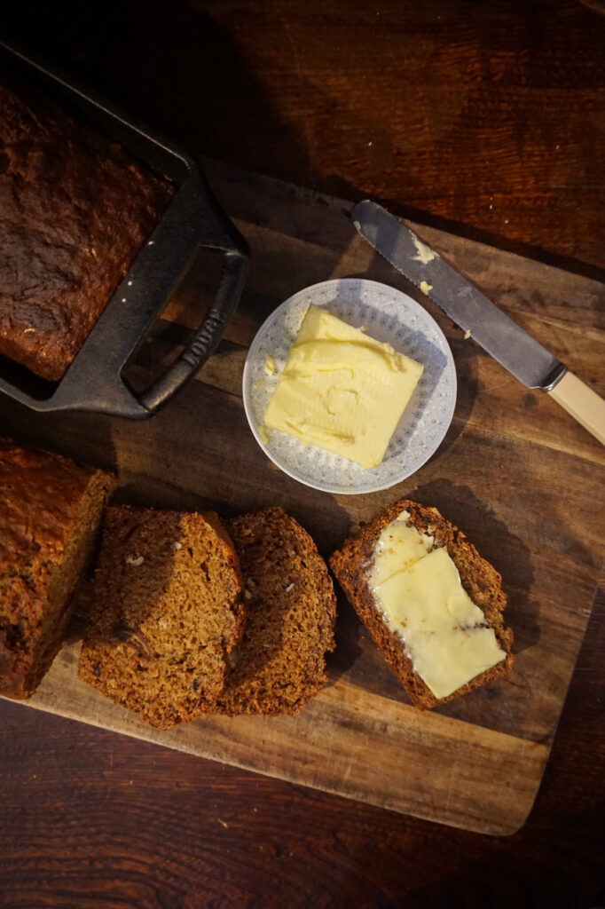 Birds eye view of a date and walnut loaf with some slices cut and a small plate of butter.