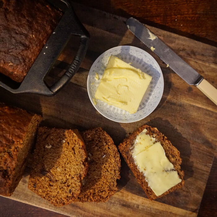 Birds eye view of a date and walnut loaf with some slices cut and a small plate of butter.